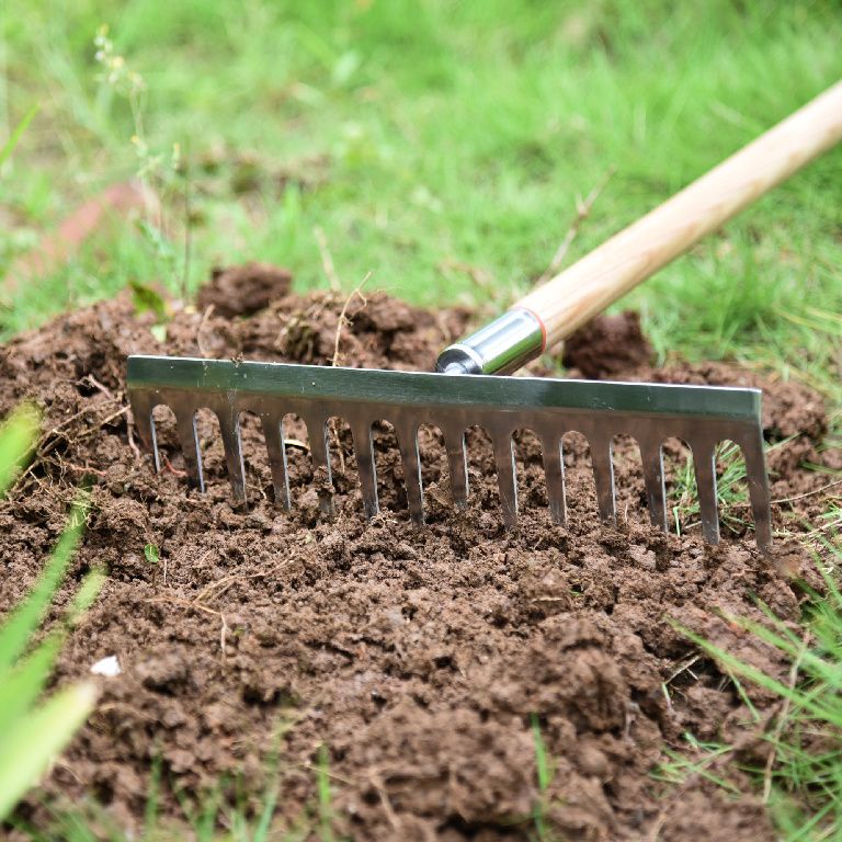 Running a metal garden rake through a patch of soil.