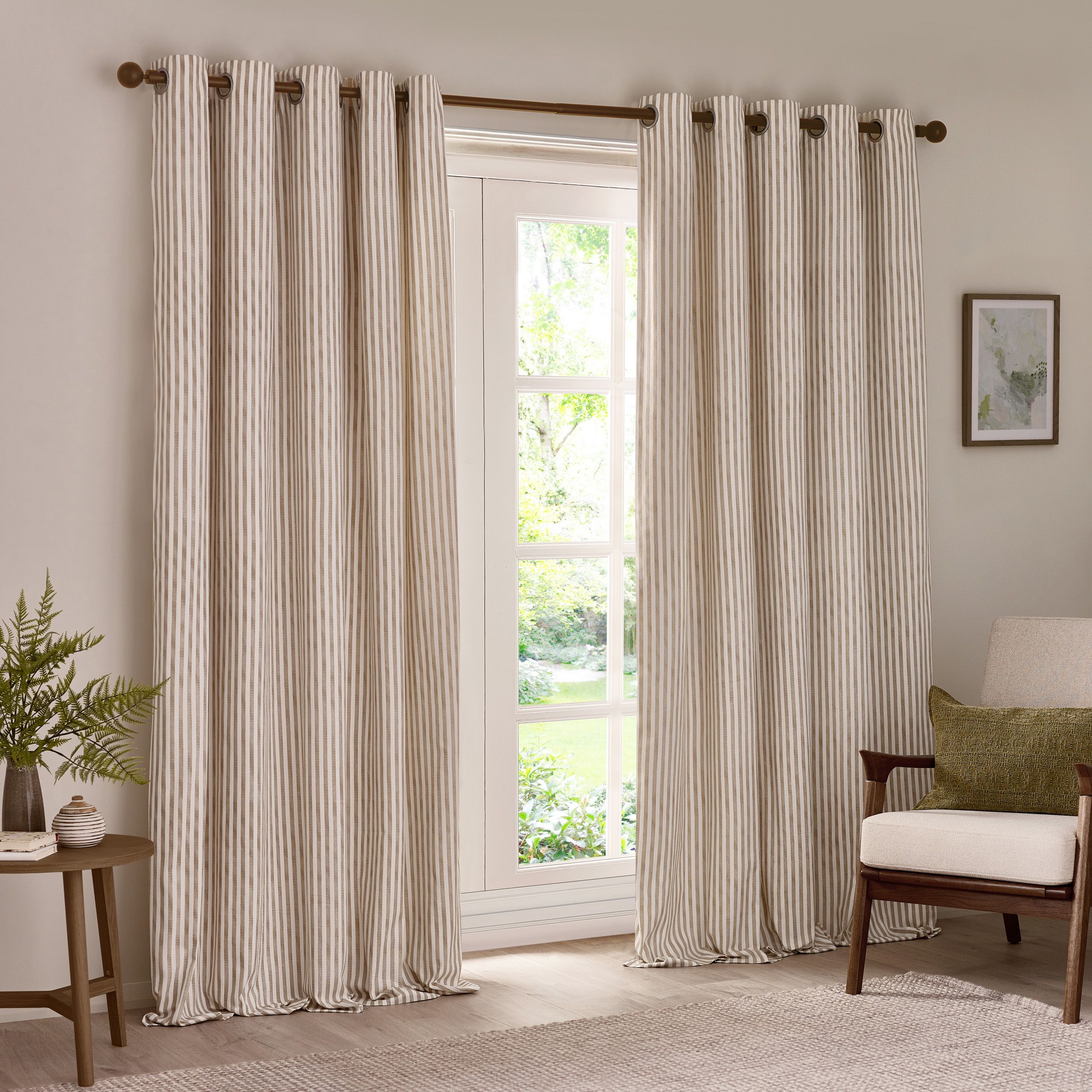 Neutral striped curtains hanging on a window in a light living room, styled with a wooden chair, green cushion and side table with plant.