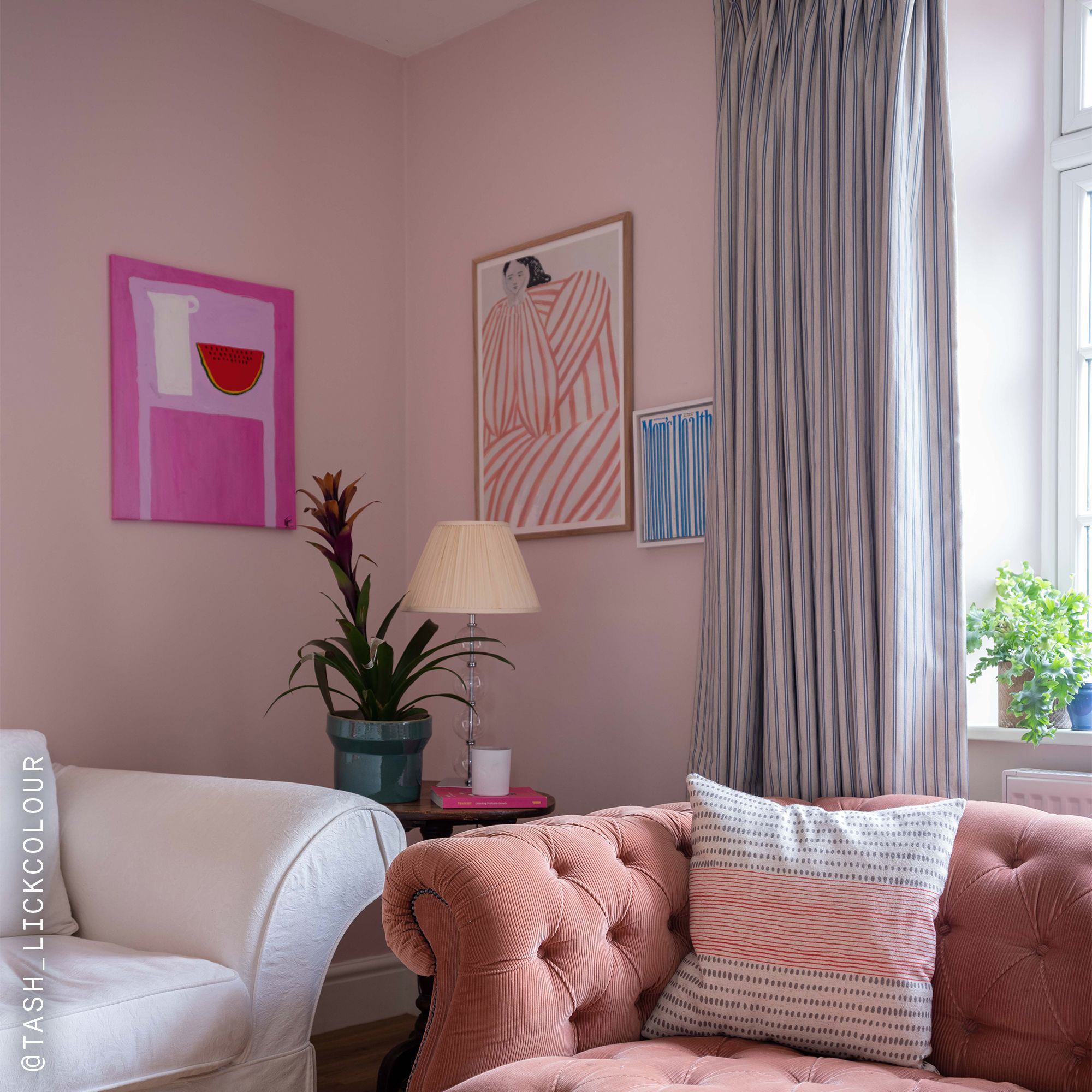 Living room with Lick Pink 05 painted walls in a soft blush tone, featuring a pink tufted sofa, a white armchair, striped curtains, framed artwork, and a side table with a lamp and houseplant creating a warm, stylish setting.