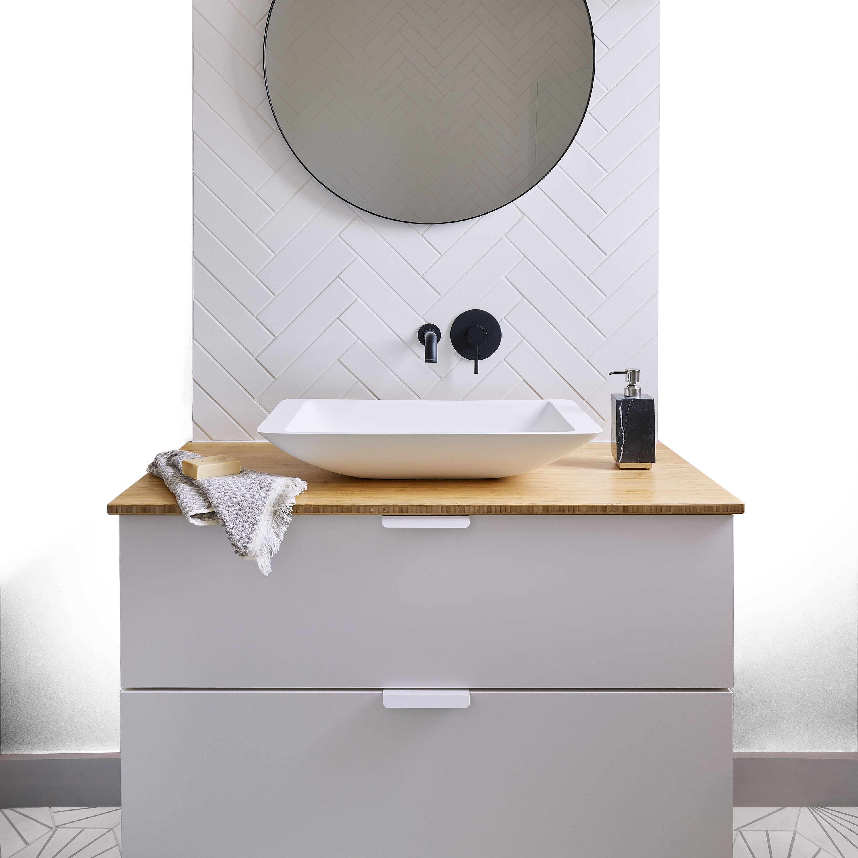 Bathroom with Valspar Mellow Mango painted walls in a warm peach tone, featuring a white vanity unit with a wooden worktop, round wall mirror, black tap fittings, and white herringbone tiles for a clean, contemporary look.