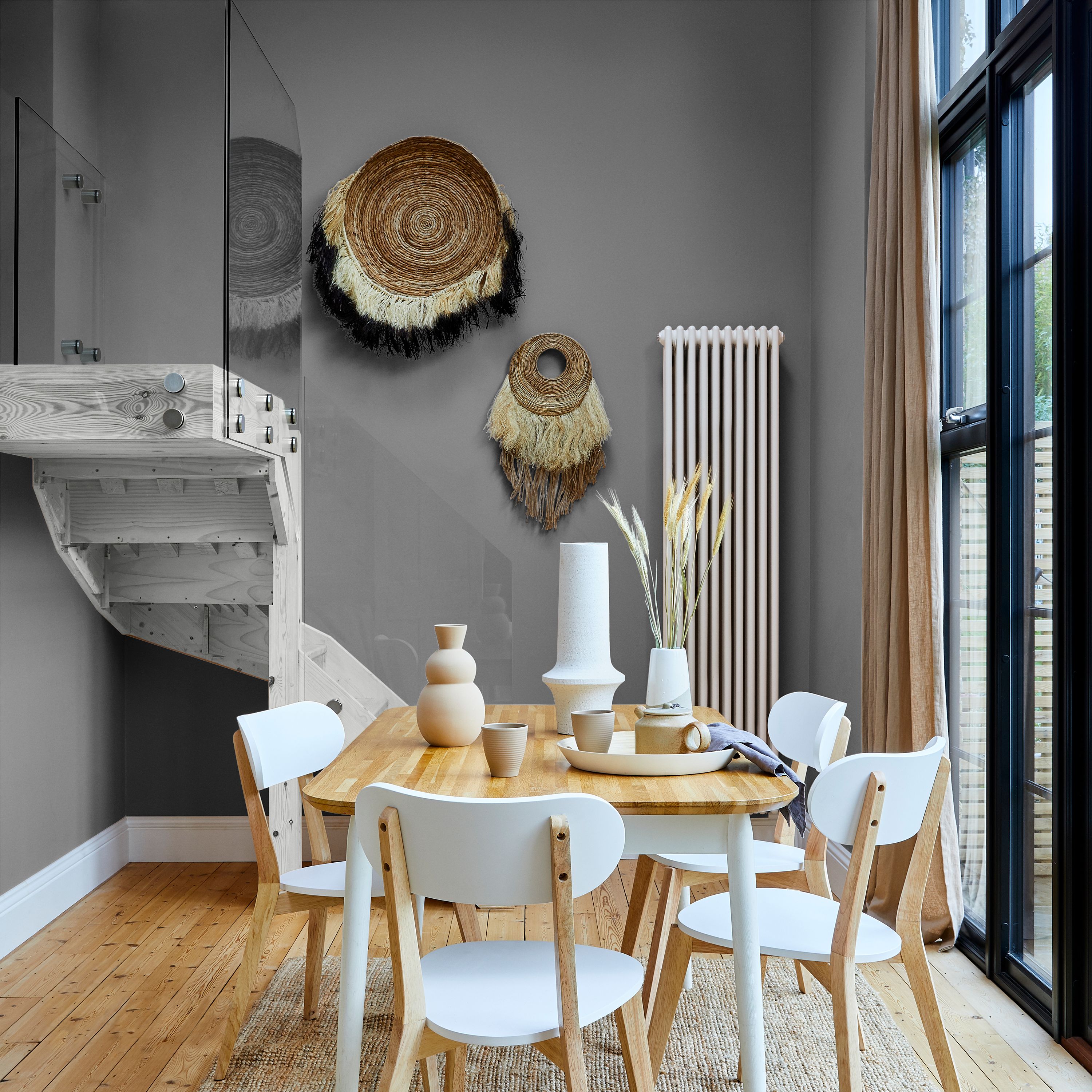 Dining area with Valspar Rugged Olive painted walls, featuring a wooden table with white chairs, styled with neutral ceramic vases, woven wall décor, light wood flooring, and large windows with beige curtains letting in natural light.