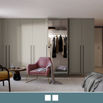 A bedroom featuring a fitted wardrobe with slab style doors finished in an elegant pebble colour and finished with modern style black handles.