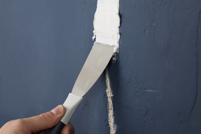 Spreading filler across a crack in a wall using a decorators knife. Filler is spread slightly wider than the width of the crack.