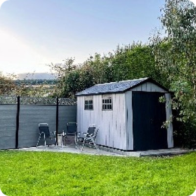 A grey garden shed with a dark double door and two windows sits neatly in a grassy backyard, surrounded by trees and wooden fencing. The shed is part of real-life garden inspiration shared by users on Instagram with the handle @fixingupforthsix