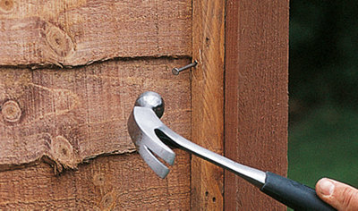 Close up of a hammer positioned above a nail, ready to drive it through a fence panel into the fence post.