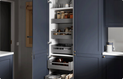 Tall shaker style kitchen cupboards have been opened to reveal the contents. There is white shelving and grey open-top drawers to allow for taller items to be stored. The inside of the cupboard is white and the fronts and backs of the cabinets are dark blue.