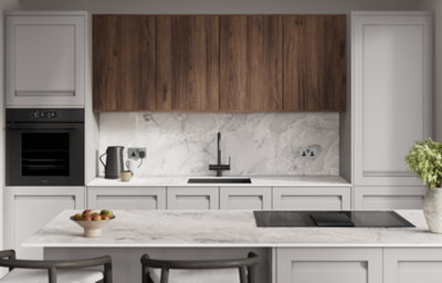 A chrome sink with mixer tap is nestled within a white and grey marble-effect countertop. The sink features a white drainage caddy and bowls and cutlery are placed to the side.