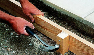 Hammering nails through a timber peg into a timber support for a drainage channel.