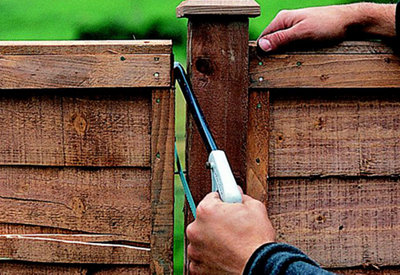 Using a hacksaw to cut through the nails which are visible in the gap between two fence panels.