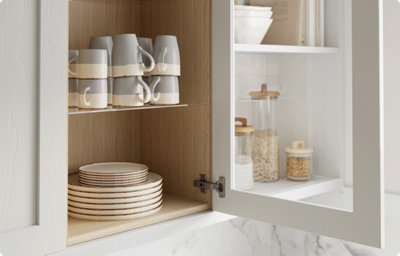 A glass-fronted cupboard door is open to reveal plates and mugs in soft shades of blue and cream.
