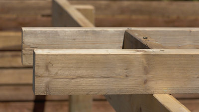 Two pergola rafters sat on top of a horizontal beam. The two rafters are separated by a timber spacer.