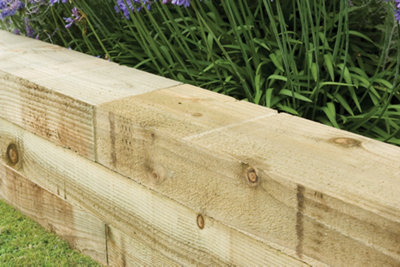 Wood railway sleeper garden border with plants behind.