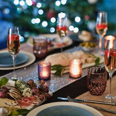 Dining table set with crockery, cutlery, champagne flutes and a charcuterie board, with twinkling lights in the blurred background creating a festive glow.