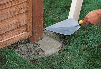 Using a trowel to smooth the concrete around the base of a fence post downwards, so water drains away from the fence post.