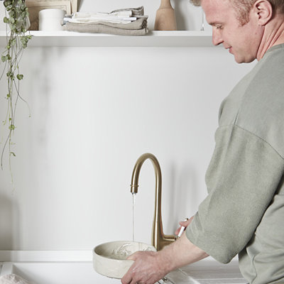 A person rinsing a bowl over a white kitchen sink installed in a minimalist kitchen space.