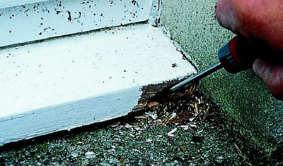 Person using a screwdriver to remove rotten wood from the corner of a wooden window sill.