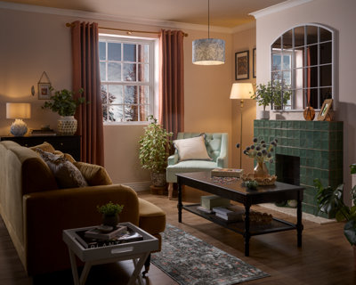 A modern bedroom with a double bed, striped bedding, throw blanket, and decorative pillows. Two wooden nightstands with lamps flank the bed. A sculptural wall piece and built-in green wardrobes are visible. A pendant light hangs overhead.