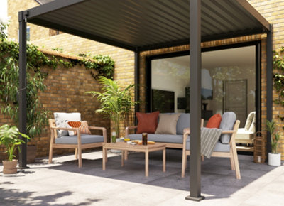 Garden party set up under a black pergola, featuring a cosy dining area with fairy lights, outdoor cushions, and lush greenery.