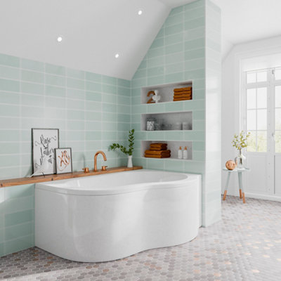 A large corner bath installed in the corner of two tiled walls. Wall behind the bath has a countertop with taps mounted on top.