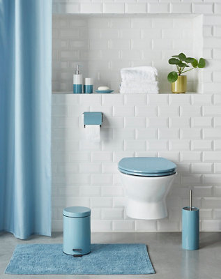A blue bath mat which complements a blue bathroom bin, toilet brush, toilet seat and toilet roll holder.