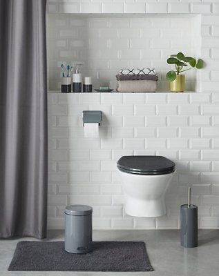 Black toilet seat fitted to a white wall hung toilet that is mounted on a white tiled wall.