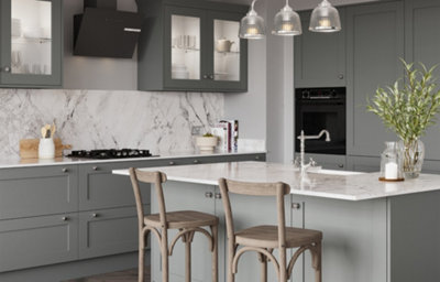 Contemporary slate grey shaker kitchen with a marble-effect splashback and island, glazed wall cabinets, integrated oven, black cooker hood, chrome tap, and wooden breakfast bar stools beneath glass pendant lights.