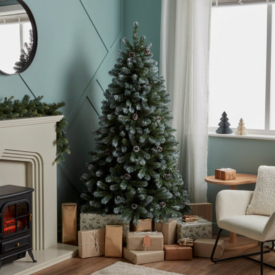 Artificial, snowy tree with pinecones, next to a fireplace with the skirt area surrounded by gifts.