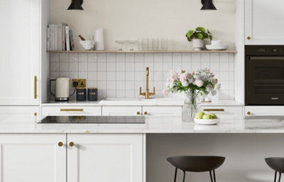 White shaker kitchen with brass handles, brass tap, marble-effect worktop, tiled splashback and integrated black oven.