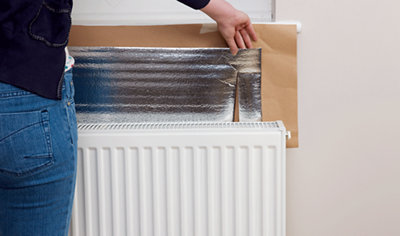 Someone sliding reflective radiator foil behind a white radiator.