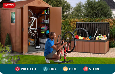 A man carries a wooden crate filled with garden tools toward an open Keter outdoor storage unit in a leafy backyard. The storage shed, with its top lid and double doors open, reveals a red lawn mower, watering cans, cushions, and a coiled hose. The scene is surrounded by greenery and flowers. Text and icons at the bottom read: "Protect," "Tidy," "Hide," and "Store."