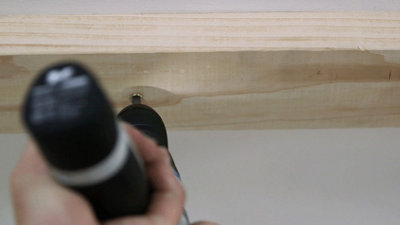 Using a drill to drive a wood screw into the the ceiling plate of a stud wall to secure it to the ceiling.