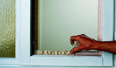 Person using their thumb to press putty into the rebate around the edge of a casement window frame.