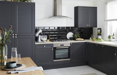 Shaker style kitchen cabinets in dark grey with a matt finish are finished with silver coloured door knobs. On the white worktop sits a fixed cabinet with a top-hinge opening. Black tiled splashback