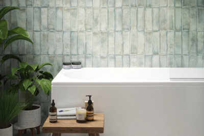 Green textured bathroom tiles above white bathtub.