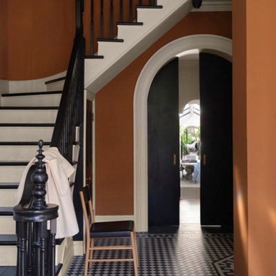 Hallway with black and white stairs, door and floor, a chair, and terracotta walls.