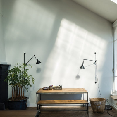 A white staircase with a dark wooden railing, beneath which is a stack of firewood, leads along a light grey wall.