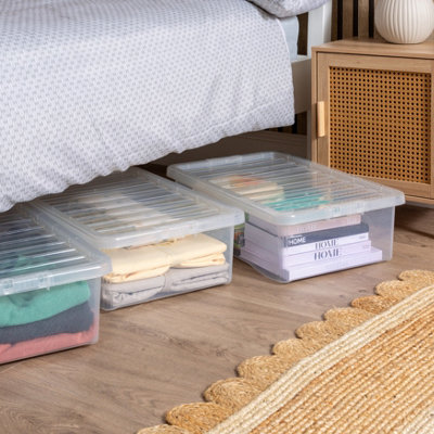 Clear plastic storage boxes filled with clothes and books under a bed.