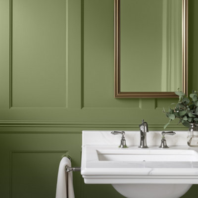 Bathroom with Lick 18 painted walls in a rich olive green, featuring classic wall panelling, a white pedestal sink with chrome taps, a hanging towel, and a framed mirror with a vase of greenery for a clean, elegant look.