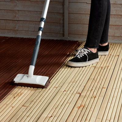 Using a paint pad on an extendable pole to apply paint to the surface of decking.
