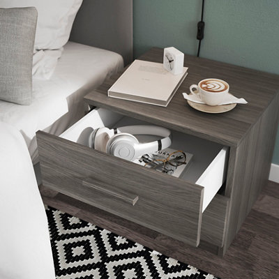 A grey wood effect bedside table with open drawers in a bedroom.