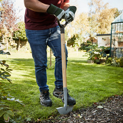 Person placing their foot on top of a half-moon edger to dig a straight line between a lawn and a flower bed.