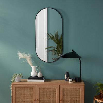 Black oval wall-mounted mirror on a teal wall above a sideboard.