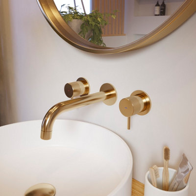 A white bathroom with a gold effect mixer tap and a gold effect round wall-mounted mirror.