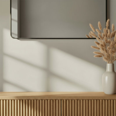 Interior vignette with GoodHome Cancun painted wall in a soft warm neutral tone, featuring a ribbed wooden sideboard topped with a ceramic vase of dried grasses, beneath a minimalist wall mirror with soft natural light casting shadows.
