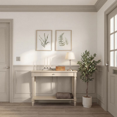 Hallway with GoodHome Tijuana painted walls in a soft warm neutral tone, featuring a light wood staircase, patterned tiled flooring, and a mid-century style console table styled with a lamp, ceramic vase, books, and framed artwork.