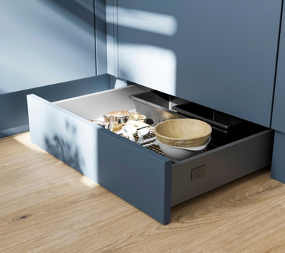 An open plinth drawer in a blue kitchen.