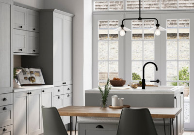 Black industrial pendant lights hanging above a shaker-style kitchen with reclaimed wooden furniture, blending bold industrial and rustic farmhouse elements.