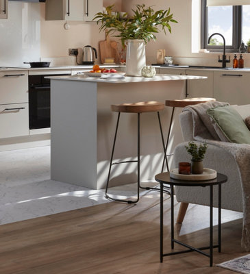 Close up of the flooring in an open plan kitchen living area. There is white marble effect flooring in the kitchen, and wooden laminate floorboards in the living area.
