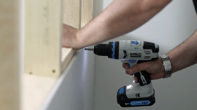 Using a drill to secure a plasterboard sheet to a timber frame with plasterboard screws. Screw is being driven in 15mm away from the edge of the plasterboard sheet.