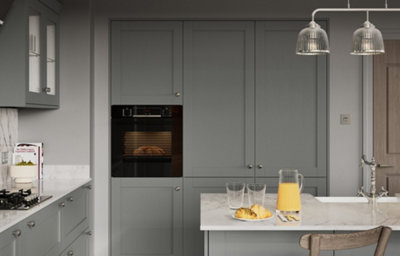 Modern slate grey shaker kitchen featuring tall cabinetry, built-in black oven, marble-effect worktops, kitchen island with breakfast pastries and orange juice, and clear glass pendant lights.